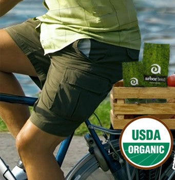 Person biking with Arbor Teas in basket and USDA Organic logo