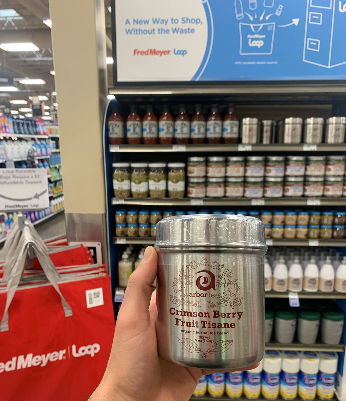Hand holding a stainless steel cansiter with Arbor Teas logo in grocery aisle