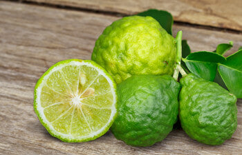 Green bergamot fruit with one cut in half on a wooden surface