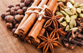 Spices including cinnamon sticks, star anise, and cloves on a wooden surface