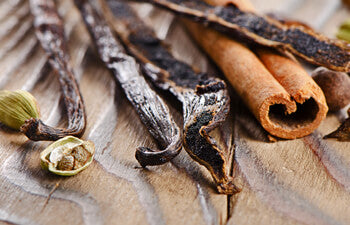 Spices including vanilla beans, cinnamon sticks, and cardamom pods on a wooden surface.