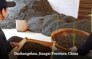 Two people handling large wooden bins filled with tea leaves in Dazhangshan, Jiangxi Province, China.