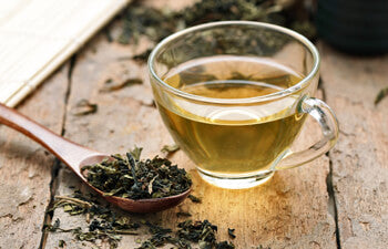 Glass cup of green tea with loose leaves in a spoon on a wooden table