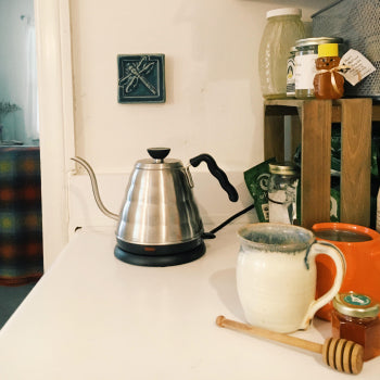 Tea-making setup with a kettle, mug, and honey dipper on a counter.