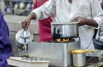 Person pouring tea from traditional metal teapot into small glasses
