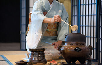 Woman in kimono on tatami mat preparing matcha for Japanese tea ceremony