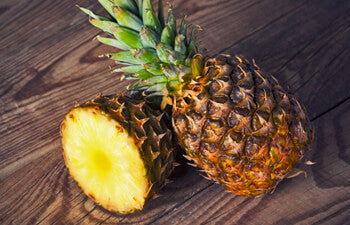Whole pineapple and cut pineapple on wooden surface