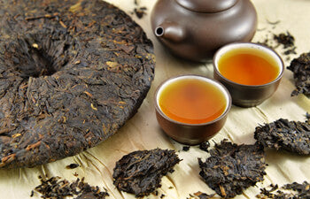 Two cups of brewed Pu-erh tea with compressed tea cake and teapot