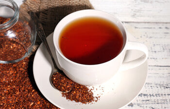 cup of brewed rooibos with loose red rooibos on saucer and table