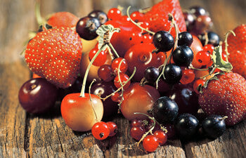 Assorted berries including strawberries, currants, and cherries on a wooden surface.