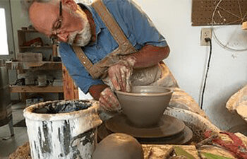 Person working with clay on a pottery wheel in a workshop.