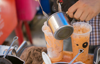 Thai iced tea being poured into two tall glasses with ice