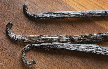 Three vanilla beans on a wooden surface