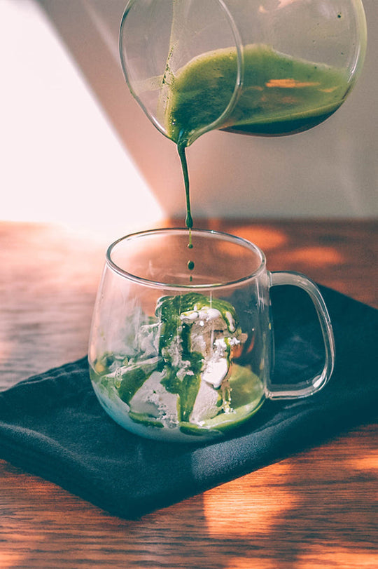 Matcha poured over vanilla ice cream in a glass