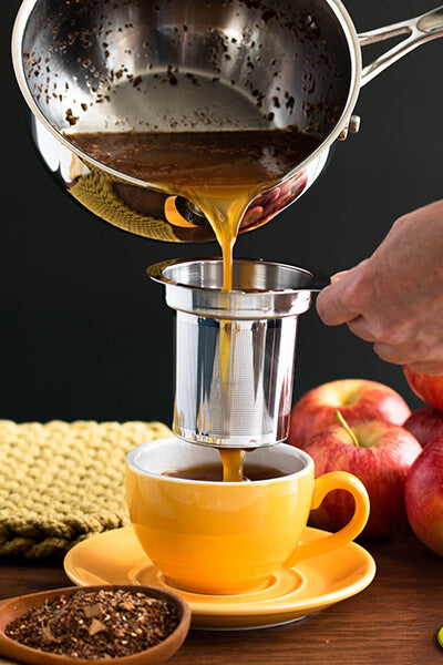 Spiced cider poured through a sieve into a yellow mug
