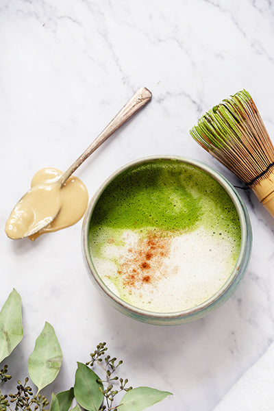 Bowl of Tahini Matcha Latte artfully displayed with spoon and Matcha whisk