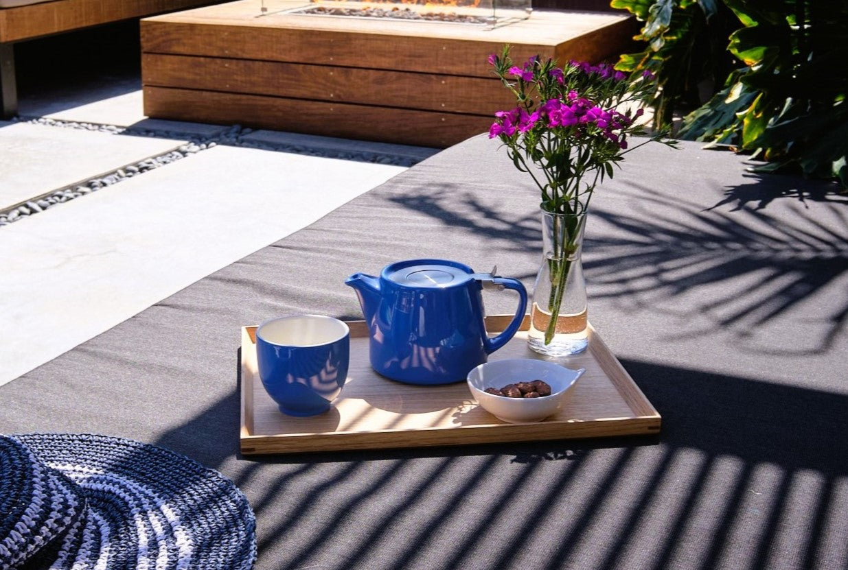 Tea set with a blue Stump teapot and cup on a wooden tray outdoors.