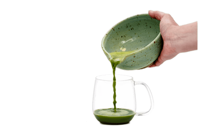 Hand pouring matcha from a ceramic bowl into a glass mug