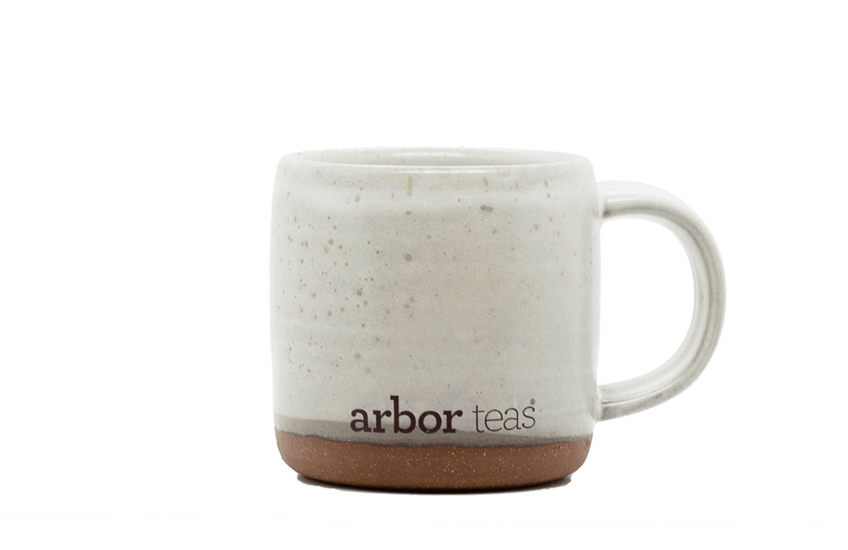 White ceramic mug with speckled pattern and 'arbor teas' branding on a black background