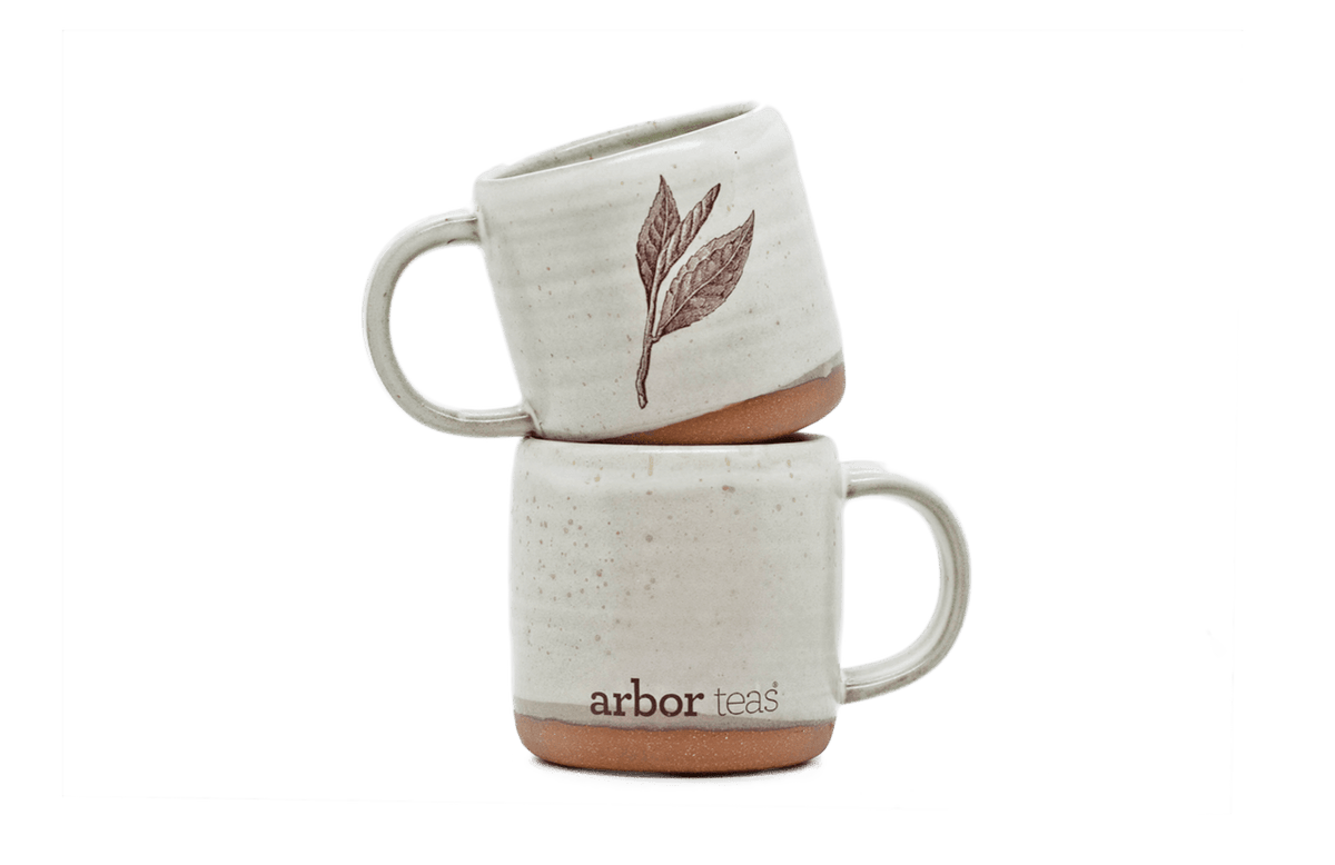 Two stacked ceramic mugs with a leaf design and 'arbor teas' branding 