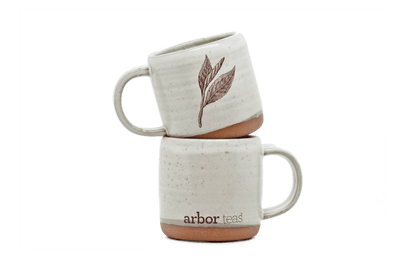 Two stacked ceramic mugs with a leaf design and 'arbor teas' branding 