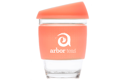 Clear glass tumbler with a coral-colored sleeve featuring the 'arbor teas' logo 