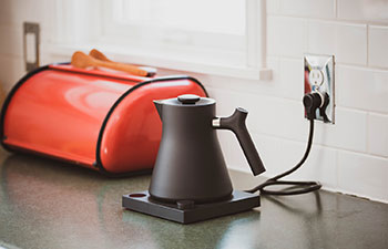 Black electric kettle on a kitchen counter with a red bread box in the background.