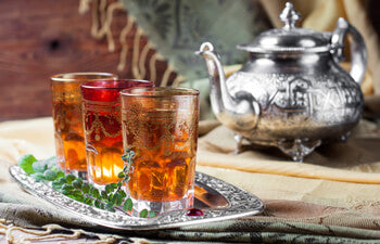 Three glasses of moroccan mint tea on a silver tray with silver teapot in background