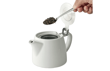 White ceramic teapot with spoon adding tea leaves into infuser