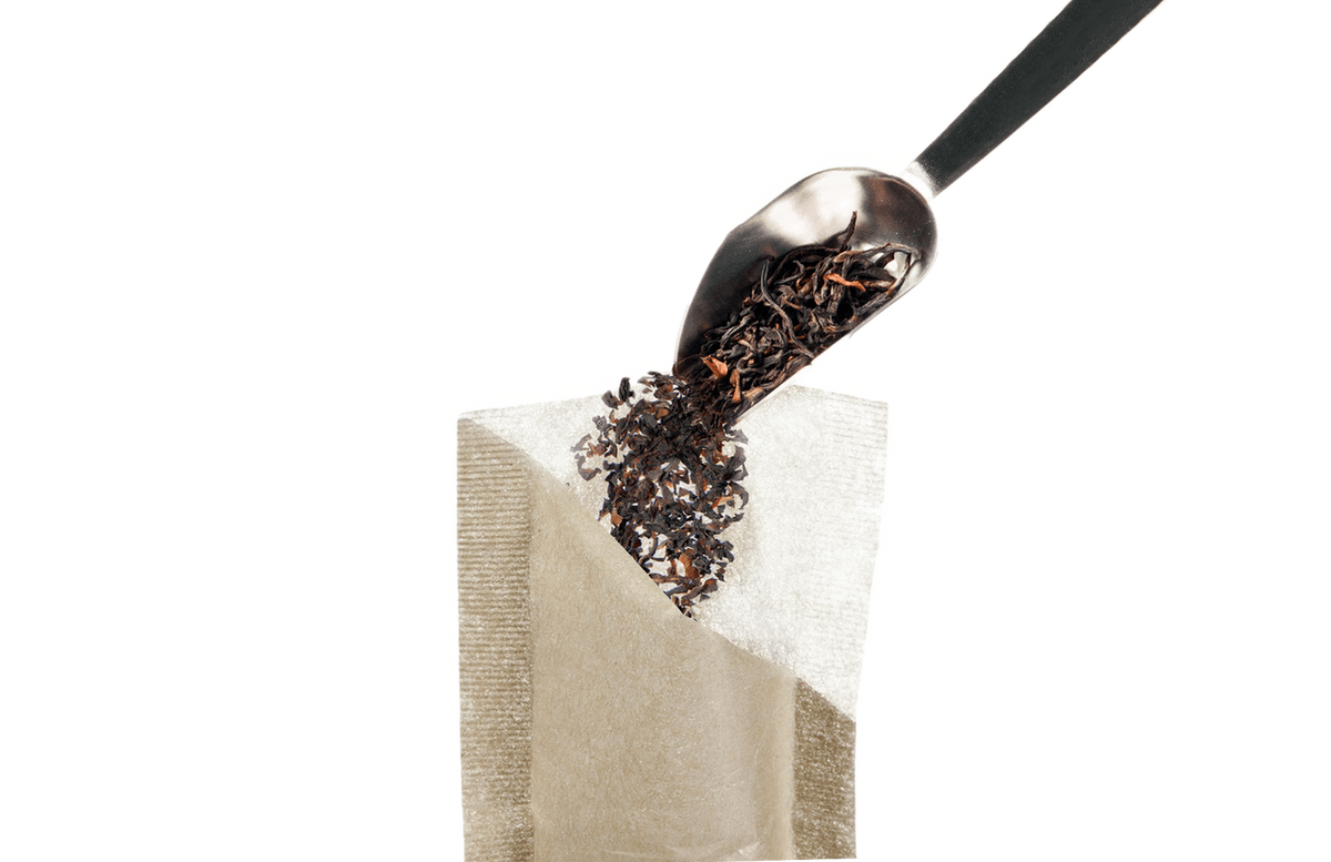 Tea leaves being poured from a spoon into a tea bag