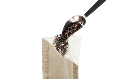 Tea leaves being poured from a spoon into a tea bag